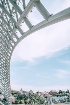 从格鲁吉亚第比利斯现代和平桥的著名钢框架下方俯瞰，可见部分阴天，覆盖着玻璃