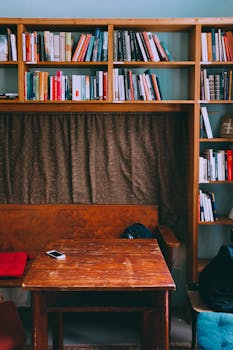 国内图书馆里，破旧的木桌和现代智能手机摆放在长凳和椅子之间，椅子上有垫子，旁边还有旧书架