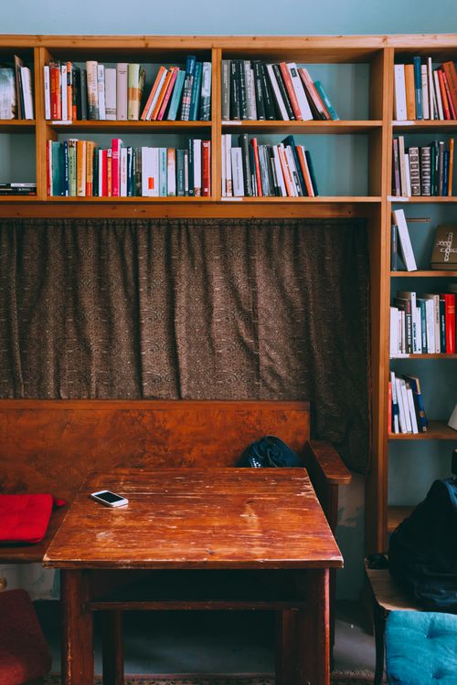 Free Domestic library interior with shabby wooden table with contemporary smartphone placed between bench and chairs with cushions and old bookshelves Stock Photo