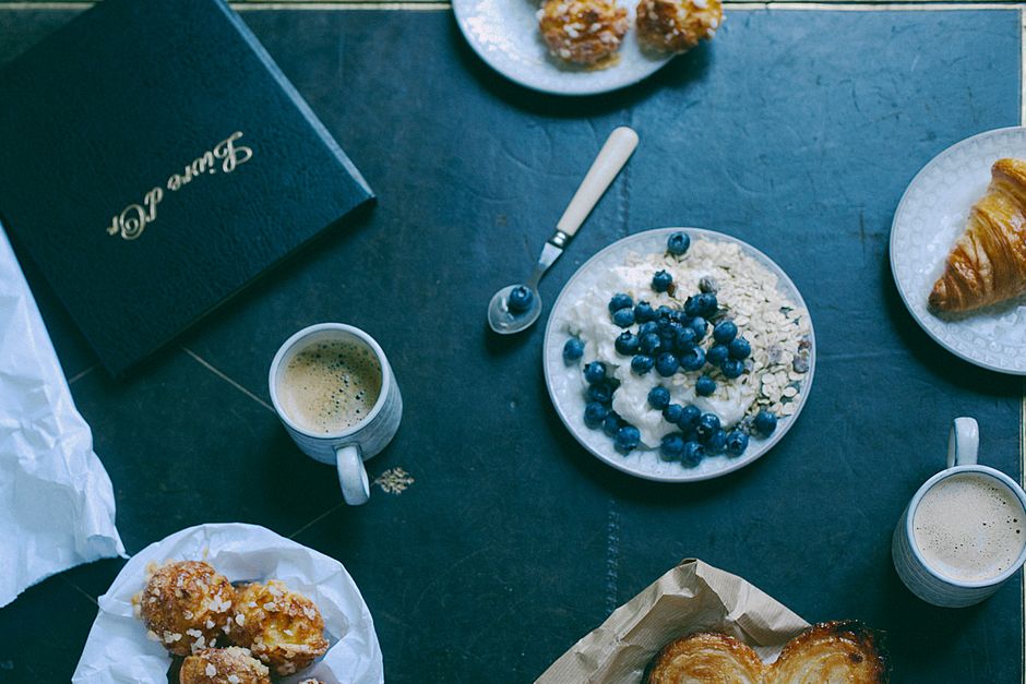 Top view of blueberry oatmeal and crispy croissants with cups of coffee for breakfast near menu in restaurant
