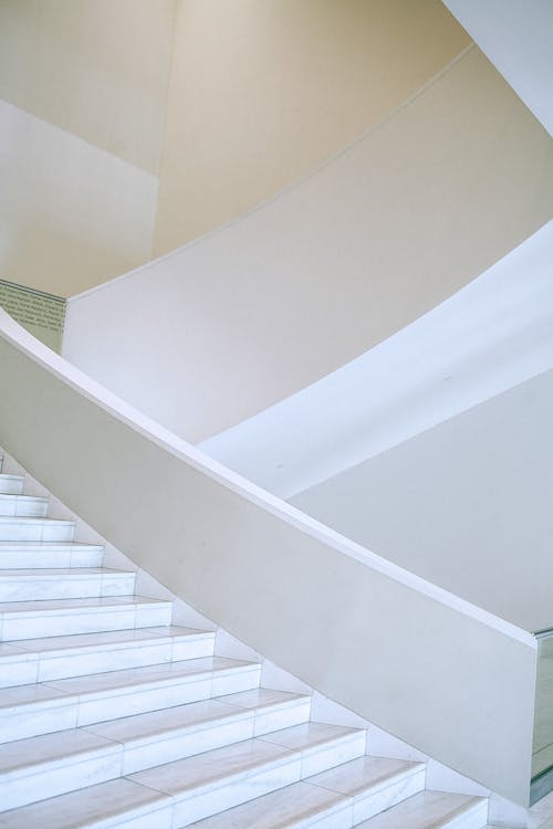 Белая бетонная винтовая лестница с белыми металлическими перилами