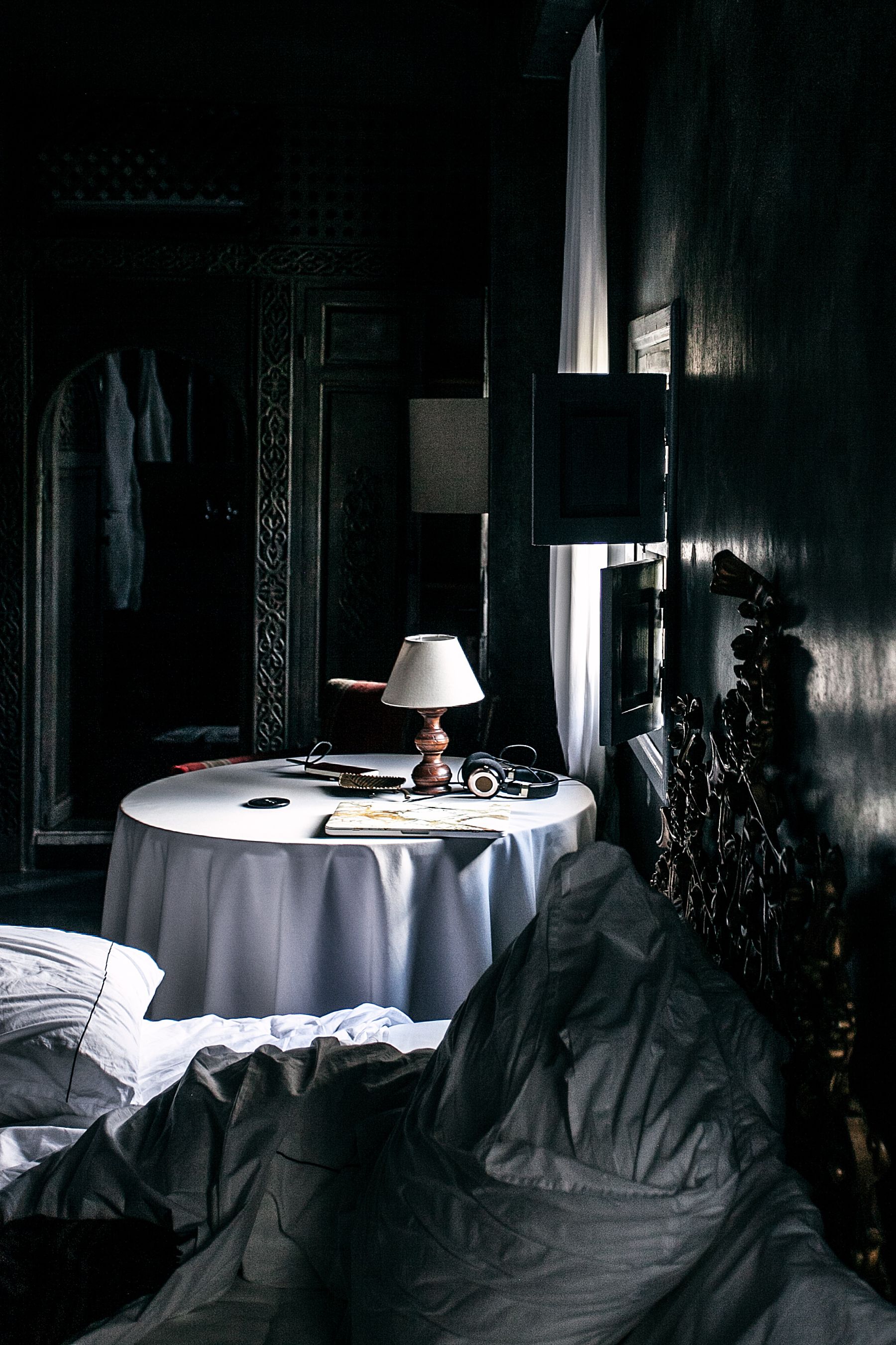 Moody bedroom with an unmade bed, dark furniture and daylight entering beside a round table