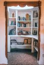 Collection of various books and decorative vases with small figures of human placed on white shelves in house