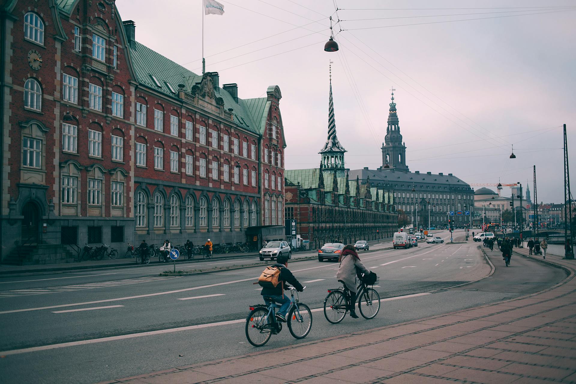 Cyclists riding along famous embankment in Copenhagen with historic Christiansborg palace and stock exchange building in Denmark on cloudy day