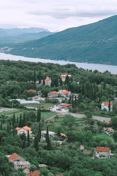 Free Aerial view of small village with modern white houses under red roofs located in lush greenery near river in front of high green mountains Stock Photo