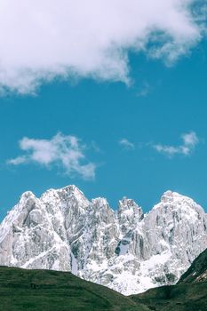 阴天之下，风景如画：绿色的山坡后方，是覆盖着积雪的粗糙岩石山脉