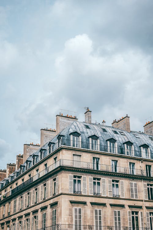 From below exterior of aged residential multistory building with slatted balconies and heating chimneys located in Paris France on cloudy day