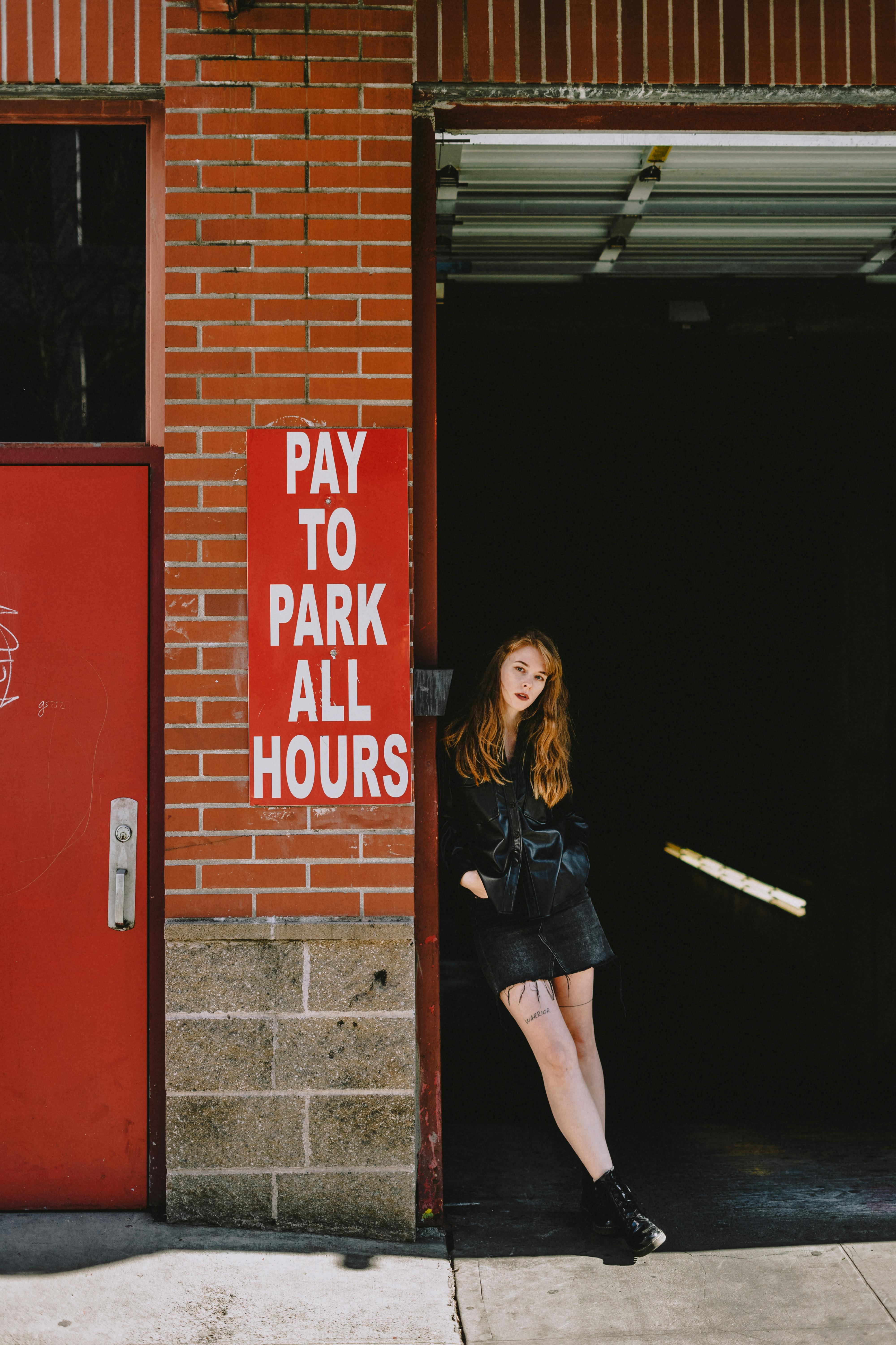 Confident young woman leaning on entrance of parking · Free Stock Photo