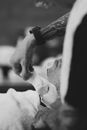 Black and white side view of crop customer covered with towel while faceless tattooed barber applying shaving foam on face during shaving procedure