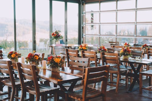 Wooden tables and chairs decorated with bouquets of colorful flowers in cozy modern cafeteria