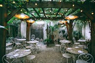 Cafe with setting on ornamental tables near chairs under decorative lamps in backyard on summer day
