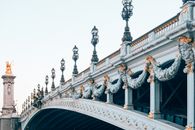 Old stone bridge with busts and row of decorative lanterns under light sky in city