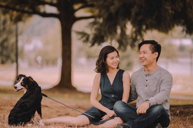 Content Asian Couple With Dog Resting In Urban Park