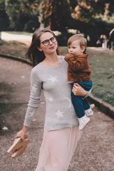一位穿着休闲服、戴着眼镜的快乐母亲抱着幼儿，手里拿着木字走在公园的小路上
