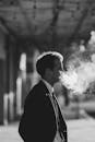 一张黑白照片里，一位穿着西装的商人在户外吐着烟