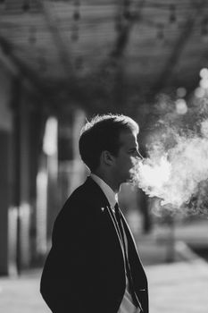 一张黑白照片里，一位穿着西装的商人在户外吐着烟