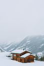 一座田园诗般的木屋坐落在白雪皑皑的山间，冬日天空朦胧