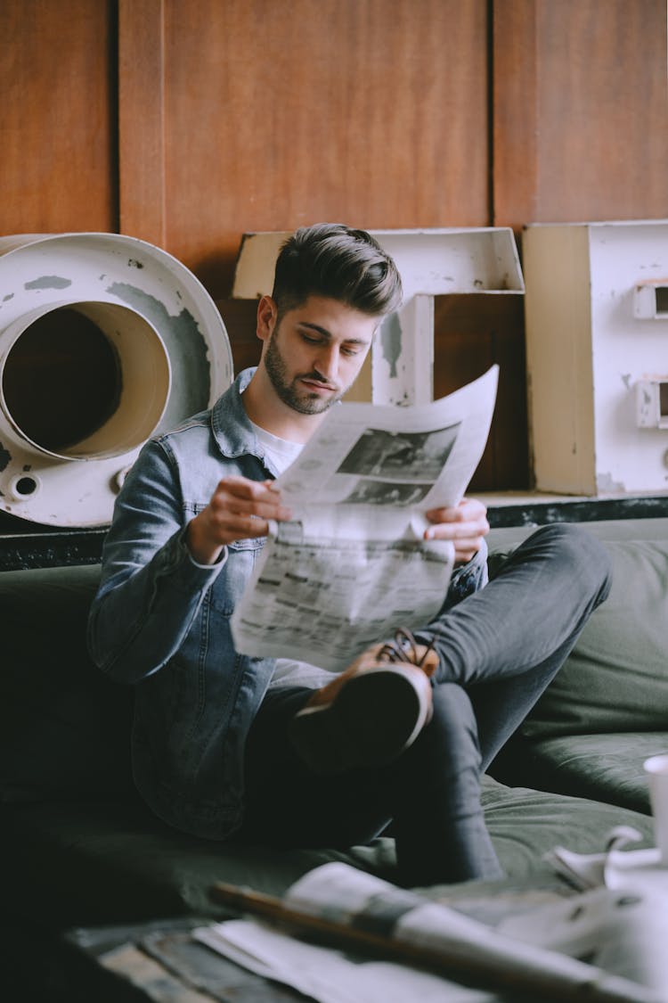 Focused Man With Newspaper In Light Room