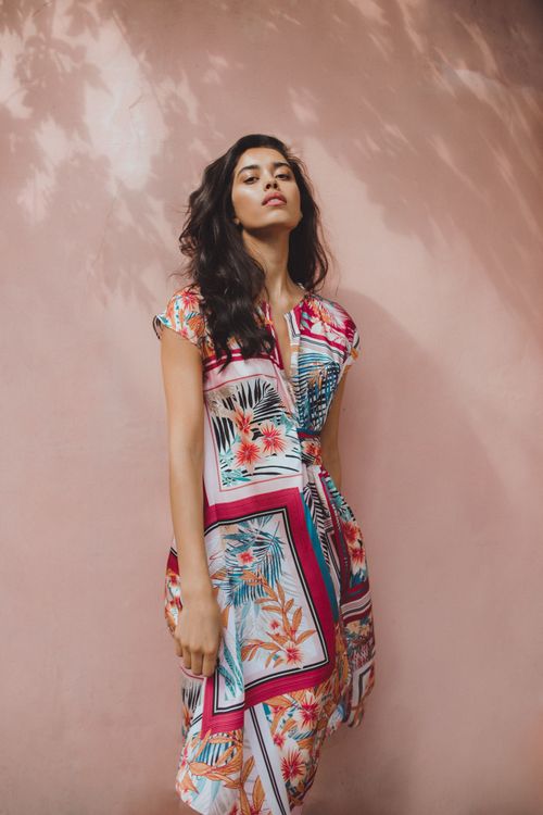 Free Low angle of young Hispanic female in summer colourful printed dress standing beside wall and looking at camera Stock Photo