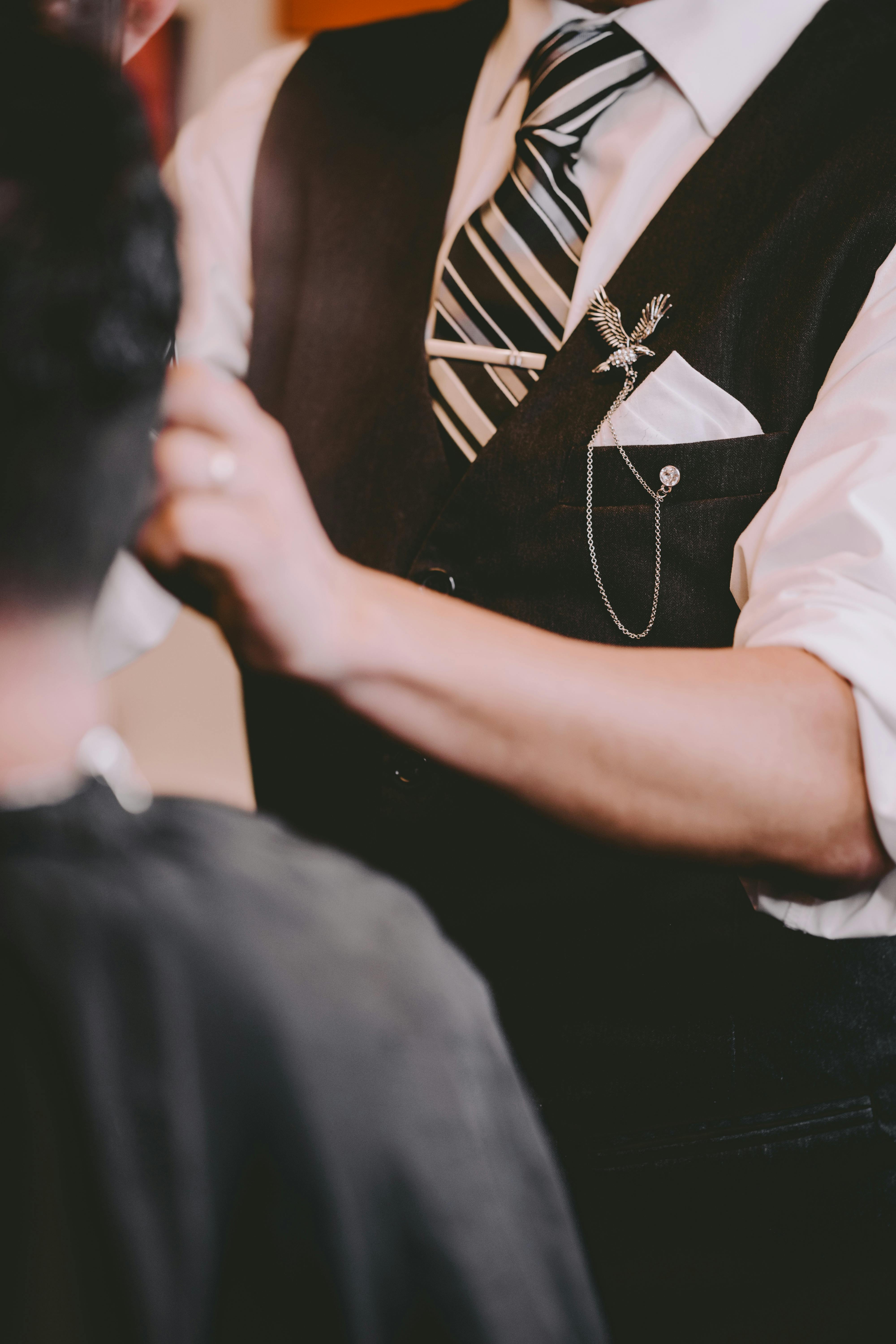 Unrecognizable stylish barber in elegant waistcoat decorated with retro brooch with chain cutting hair of client