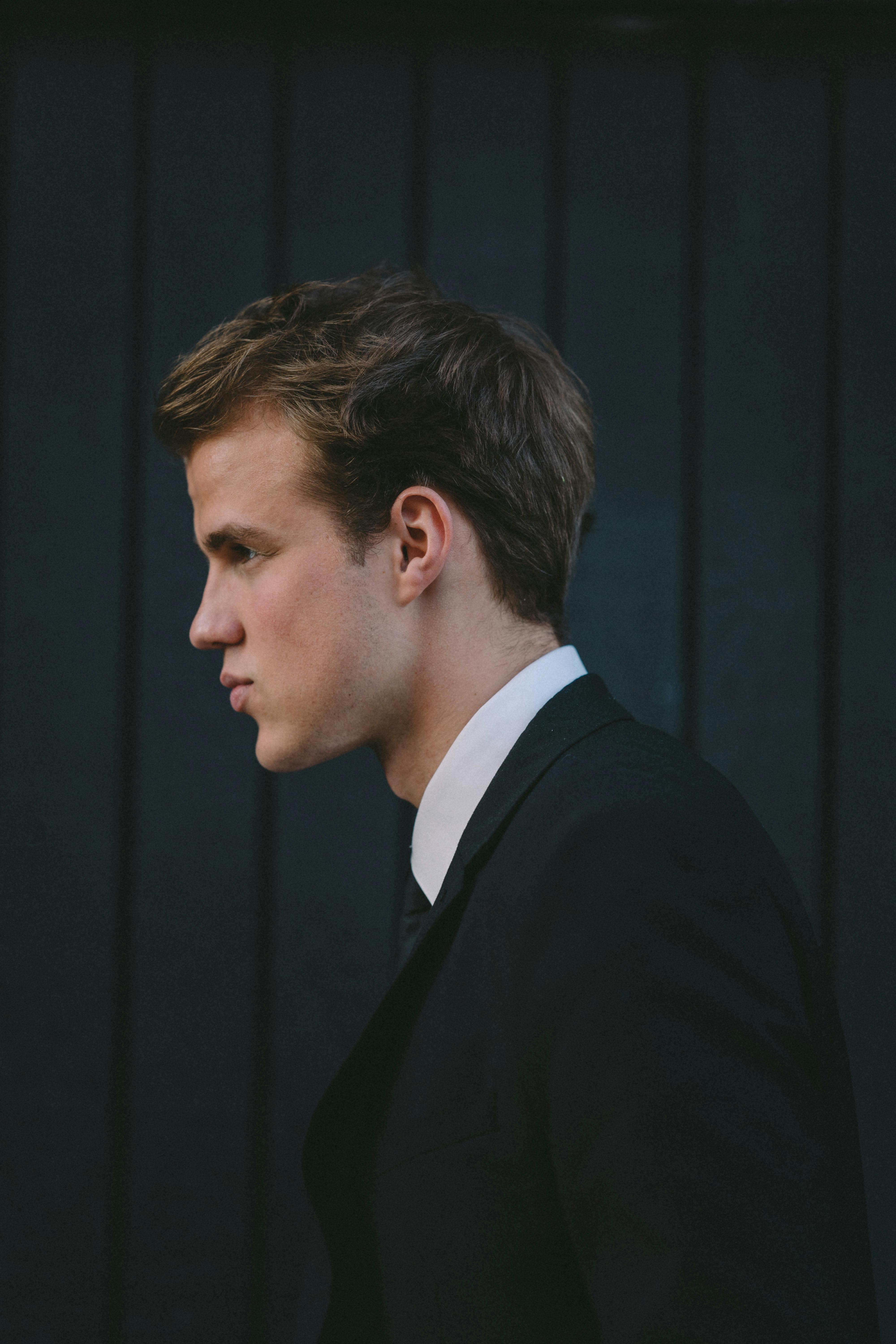 街头黑木墙附近，一位身穿经典西装的年轻帅哥的侧面图