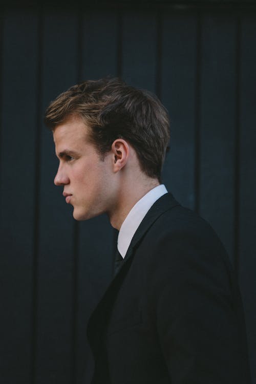 Side view of young handsome man in classic suit near black wooden wall on street
