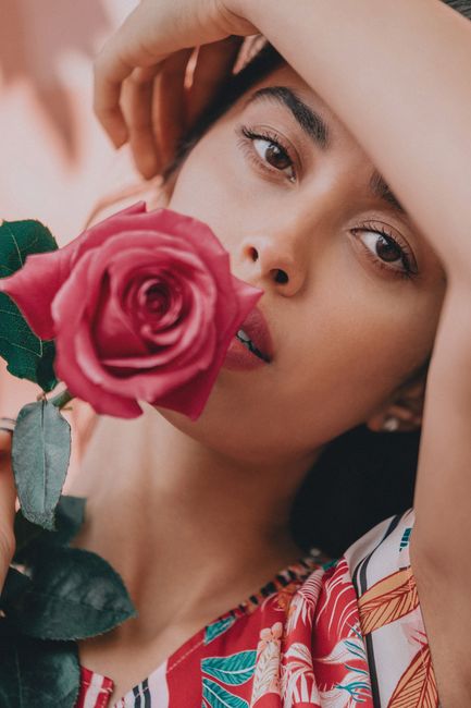 Young dreamy Hispanic female in colourful clothes with fresh rose looking at camera