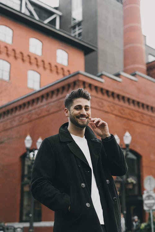 Cheerful handsome man in coat standing outside modern building