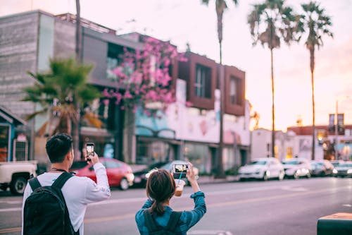 Unrecognizable tourists taking pictures on smartphone of tropical city street