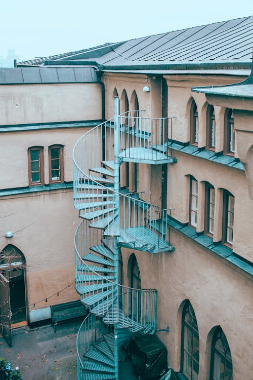 Exterior of old apartment building with outdoor spiral stairway and windows of different shapes