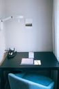 Comfortable workplace with blue cozy chair and black table with notepad phone and overhead lamp