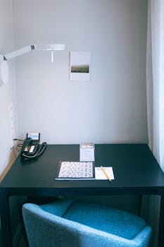 Comfortable workplace with blue cozy chair and black table with notepad phone and overhead lamp