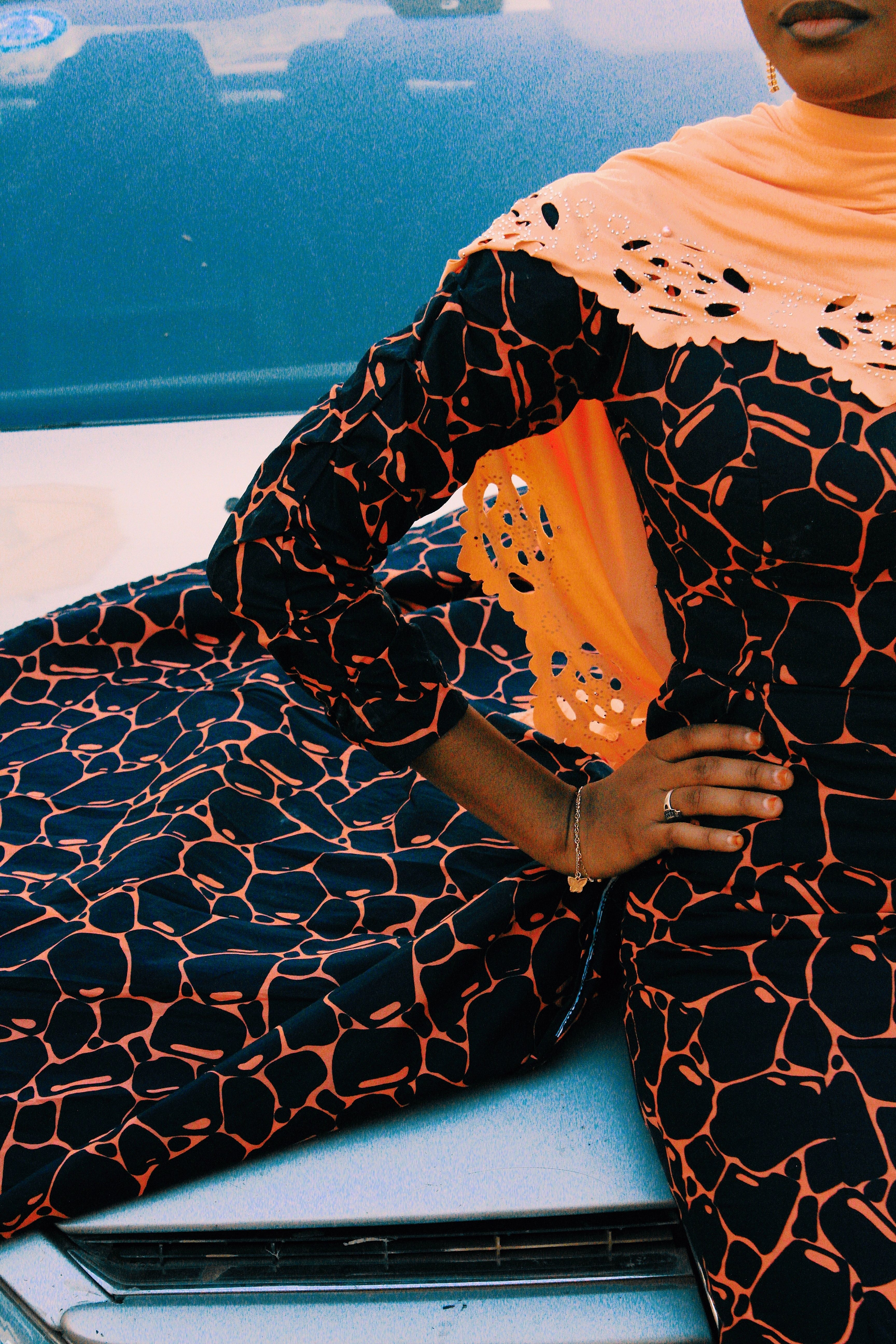 Stylish woman in patterned dress with orange scarf posing confidently outdoors.
