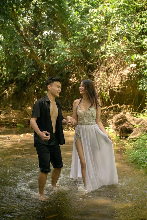 Happy ethnic couple walking in river in green forest