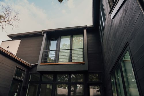 Free From below of simple open balcony of tall luxury cottage with black walls constructed of wood under cloudy sky and leafless branches Stock Photo