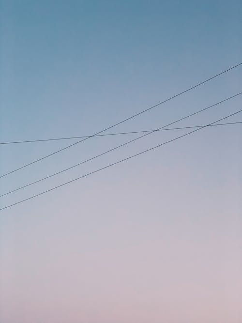 From below of thin electricity wires against blue and soft pink sky at sunset