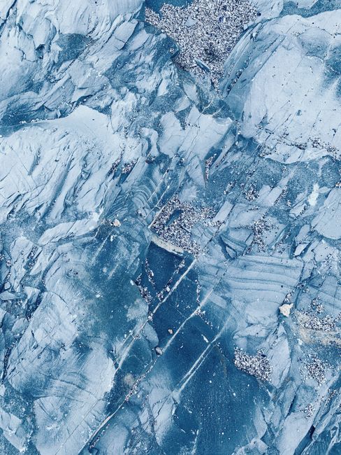 Top view of abstract background of blue frozen ice with fine pebbles in daylight