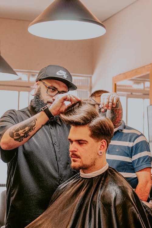 Bearded barber cutting doing haircut to male client in salon