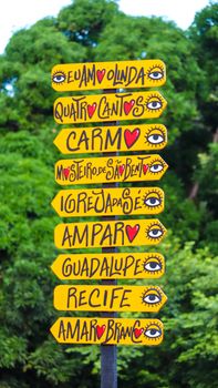 Vibrant signpost with directional arrows in Olinda, Brazil, set against greenery.