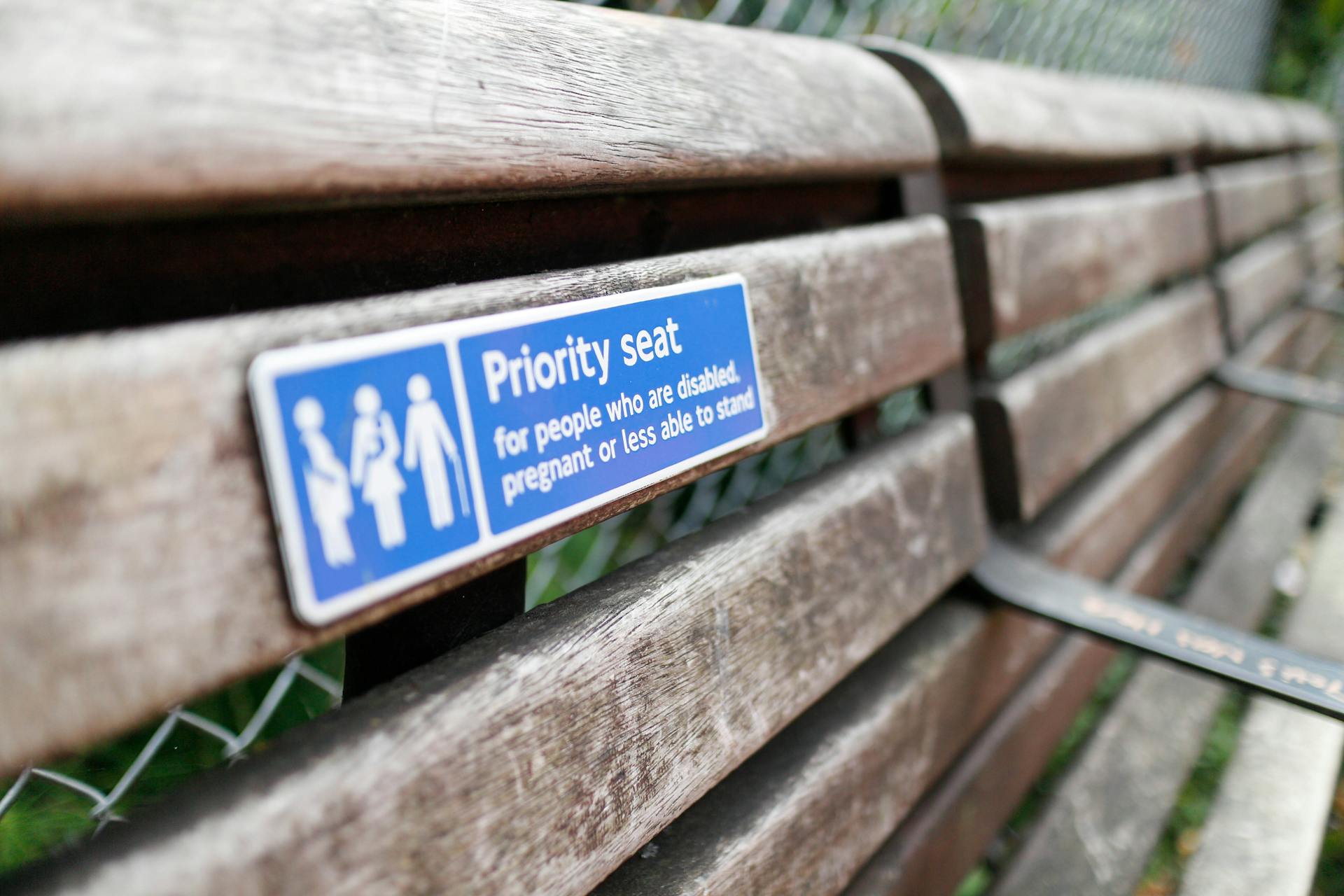 Close-up of a weathered wooden bench with a priority seating sign for disabled, pregnant individuals.