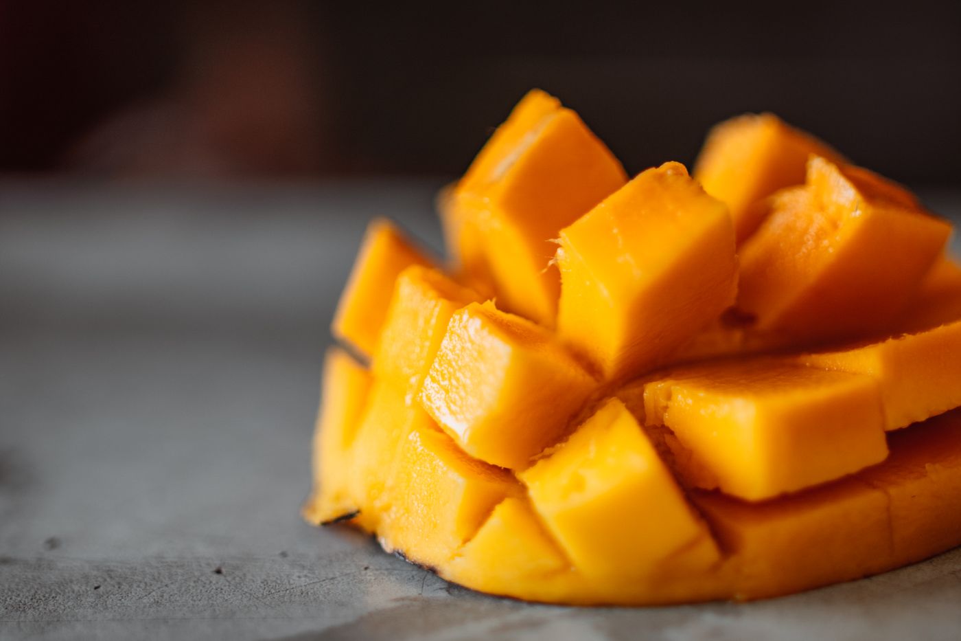 Diced ripe yellow mango cubes arranged on a gray surface