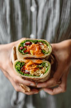 A close-up of hands holding a sliced vegetarian wrap with fresh vegetables and sauce.