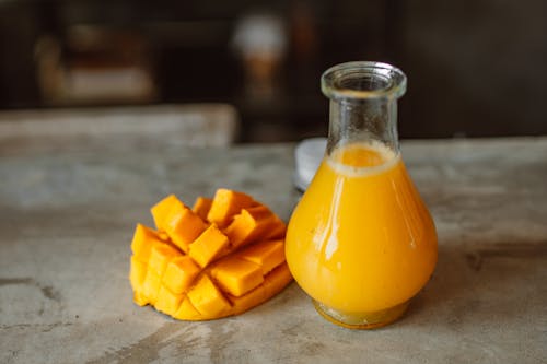 Sliced Mango Beside a Clear Glass Bottle With Yellow Liquid 