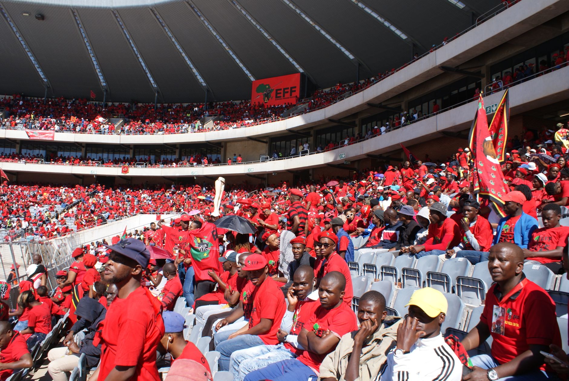 Lively crowd wearing red gathers at stadium event in Soweto, South Africa.