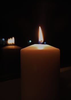 A close-up view of a candle and its flame, reflecting gently in the darkness.