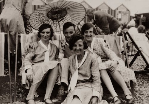Grayscale Photo of Three Women With Same Outfit  And A Man Sitting Under An Umbrella