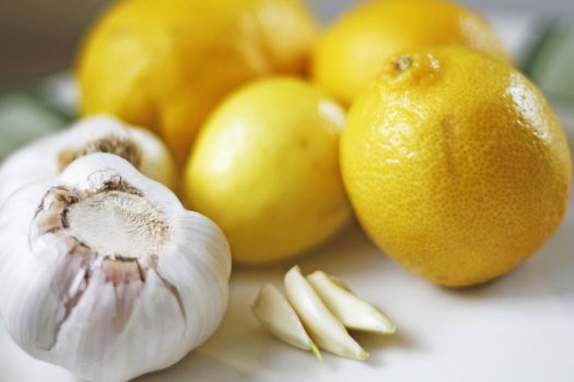 Close-up of fresh garlic bulbs and lemons on a white surface, emphasizing freshness and vibrant colors.