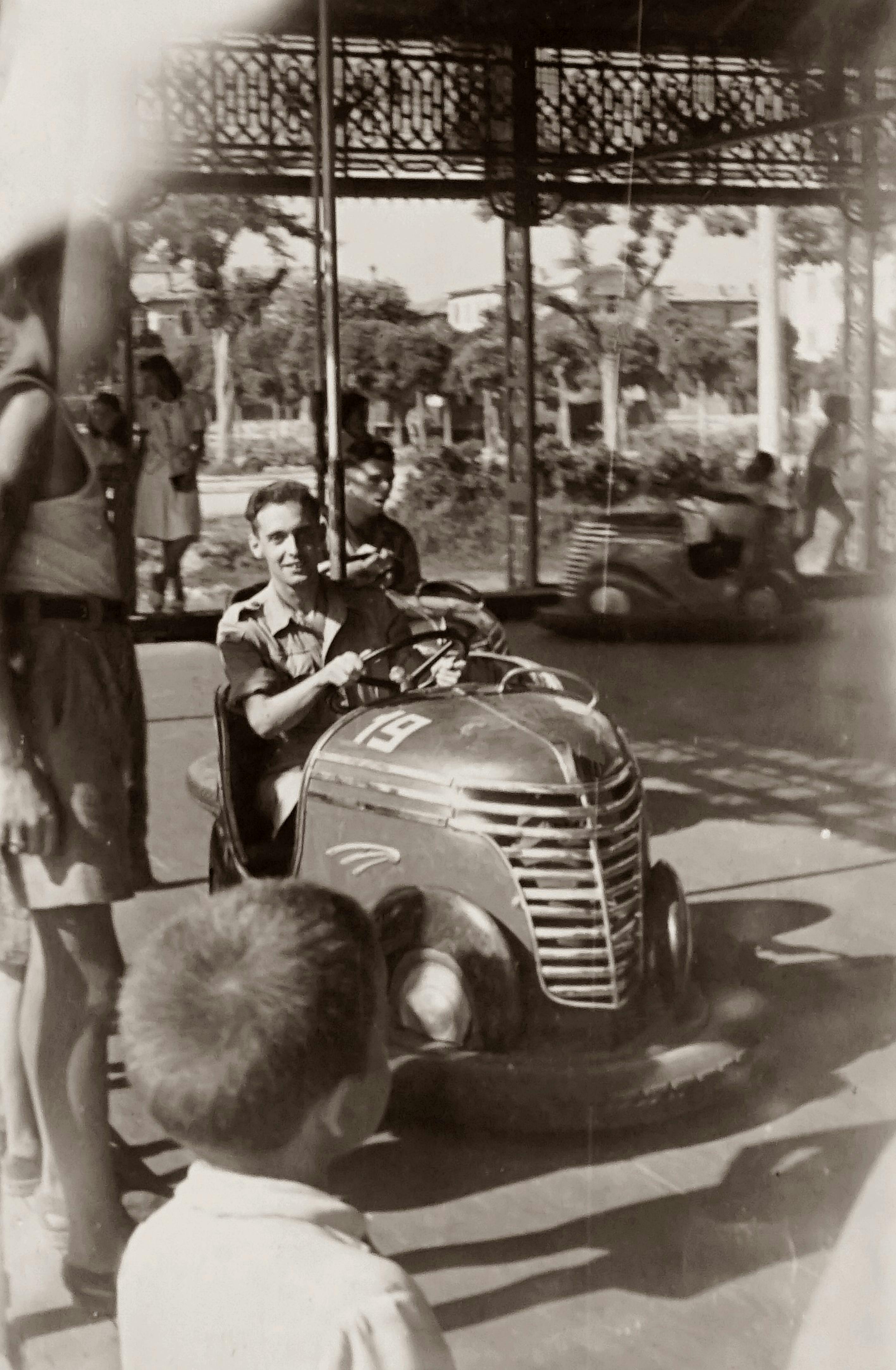 Monochrome photo of a man enjoying a classic bumper car ride at a funfair.