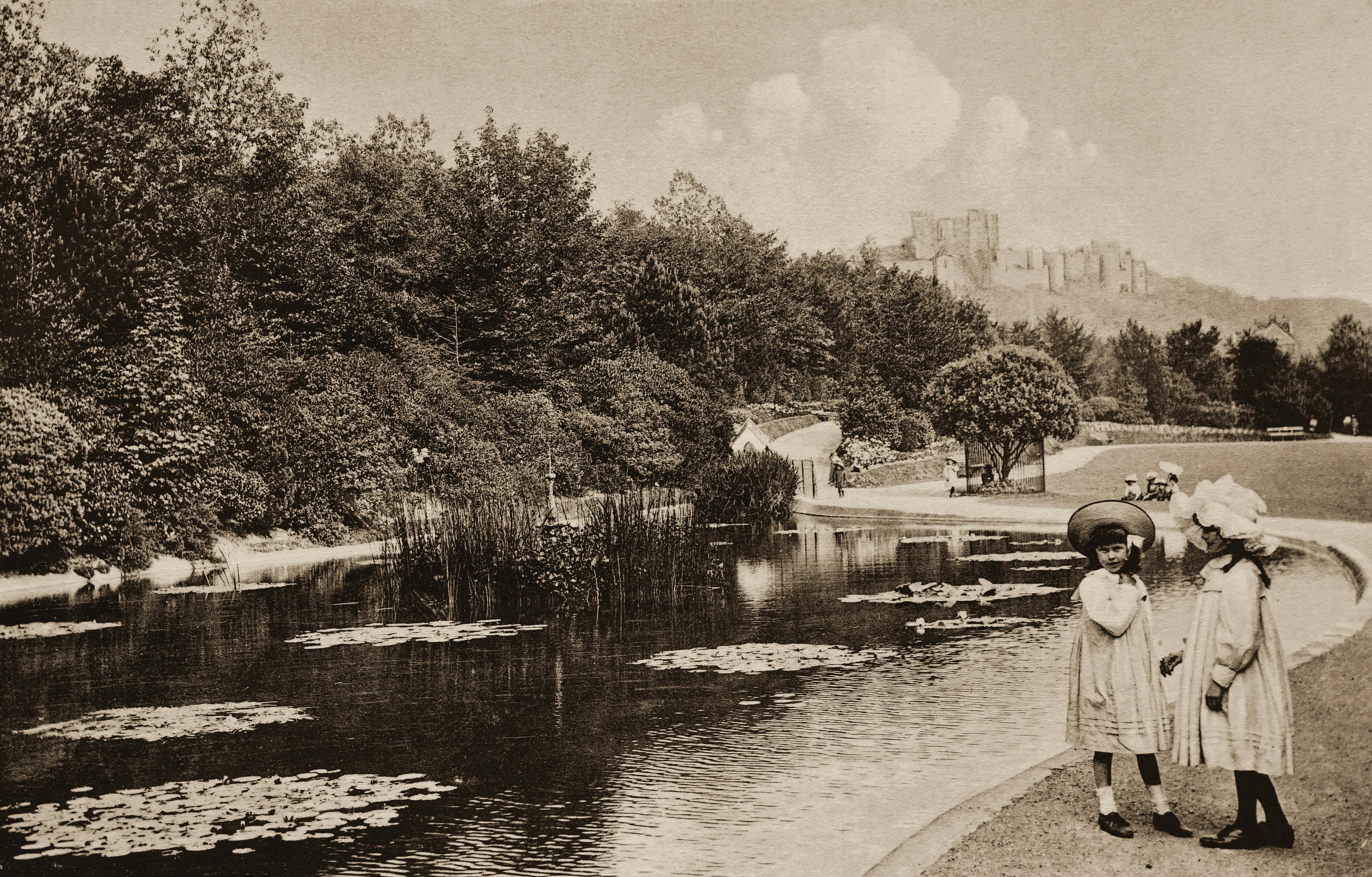 A vintage Edwardian photo of two young girls in a park by a pond, exuding classic charm.