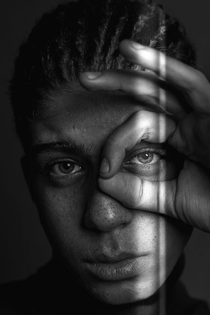 Striking black and white portrait featuring a person with freckles peering through hands.
